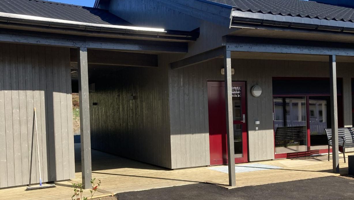 Fasade med overbygd inngangsparti, trekledning og markerte røde dører som gir et moderne uttrykk.