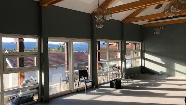 Romslig sal med skråtak, synlige trebjelker og store vindusflater mot fjellandskap.